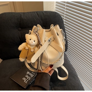 Detail of beige pebble leather bucket bag with drawstring closure and cute bear pendant