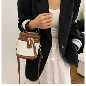 Detail of a white quilted leather bucket bag with brown trim and gold hardware on model