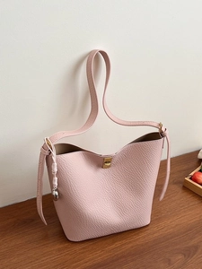 Pale pink lychee grain leather bucket bag with gold clasp and decorative woven charm
