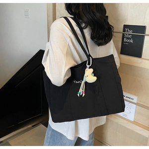 Detail of black tote bag with white lettering and a yellow moon plush pendant on shoulder