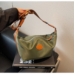 Close-up of olive green nylon dumpling bag with leather logo patch and brown strap