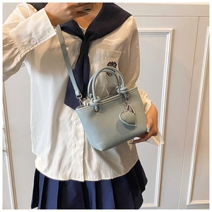 Detail of light blue bucket bag with litchi texture, knot handles and silver heart charm