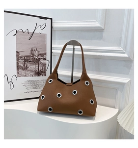 Detail of brown leather shoulder bag featuring silver metal eyelets and minimalist design