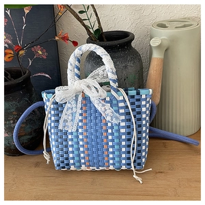 Detail of woven bucket bag with blue and orange grid pattern and a large lace bow