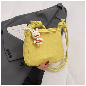 Detail of yellow lychee texture crossbody bag with astronaut bunny charm and knot strap