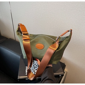 Detail of army green nylon crescent bag with brown wide strap and leather brand patch