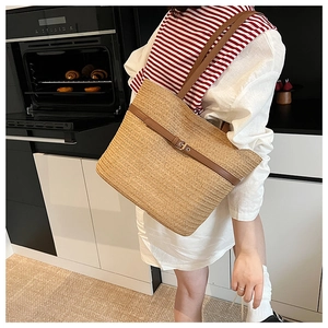 Detail of woven straw tote bag featuring brown leather straps and metal buckle accent