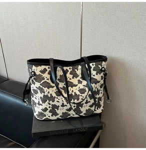 Dettaglio della borsa tote con stampa mucca, manici in pelle nera e anelli in metallo