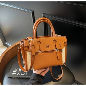 Detail of a brown leather and beige canvas tote bag with metal buckle and shoulder strap