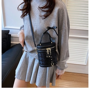 Detail of black cylindrical bucket bag featuring quilted texture and ribbon bow