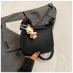 Detail of black pebbled leather bucket bag with knot strap and cute bunny charm