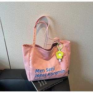 Detailed view of pink canvas tote bag with blue embroidery and yellow flower charm decoration