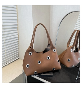 Close-up of caramel brown leather shoulder bag with silver eyelet details and litchi texture