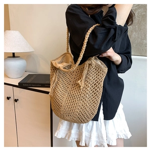 Close-up of beige woven tote bag featuring decorative tassels and braided handles