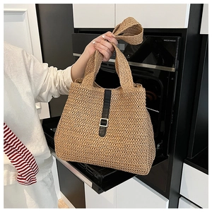 Détail d'un sac cabas en paille tissé avec lanières en cuir noir et boucles dorées