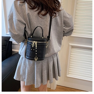 Detail of black cylindrical bucket bag featuring quilted PU leather and gold metal zipper