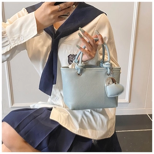 Detail of light blue lychee-textured bucket bag with knot handles and heart charm