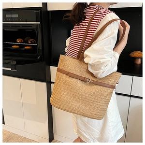Close-up of hand-woven straw tote bag with brown leather handles and metal buckle detail