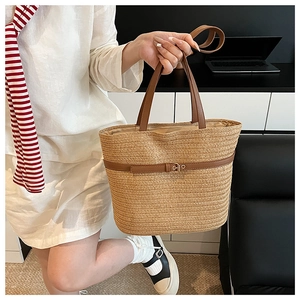 Detail view of woven straw tote bag featuring brown leather handles and metal buckle strap