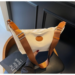 Detail of beige nylon dumpling bag with adjustable brown wide shoulder strap and leather patch