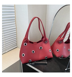 Detail of red pebbled leather shoulder bag with decorative silver metal eyelets and handle