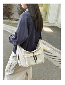 Outdoor shot of a beige nylon crossbody bag with multi-pocket utility design on a model