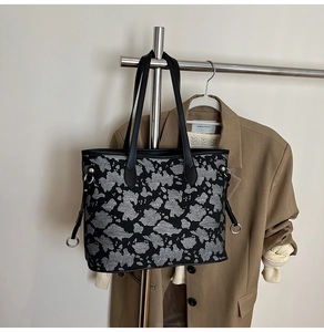 Dettaglio di una borsa tote grigia testurizzata con manici in pelle nera e anelli argento