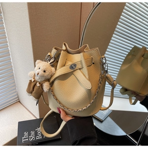 Mirror reflection showing a beige bucket bag with litchi texture and a cute bear charm