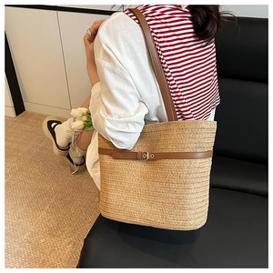 Detail of woven straw tote bag with brown leather strap and golden buckle accent