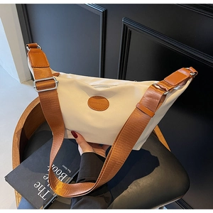 Detail of crescent oxford bag showing the brown logo patch and adjustable wide strap