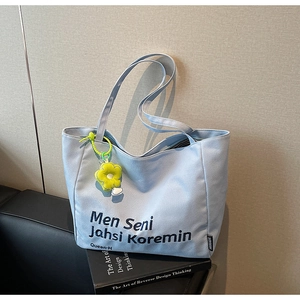 Light blue canvas tote bag with black embroidery and yellow flower pendant on a sofa