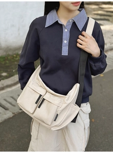 Detail of a beige nylon crossbody bag with dual utility pockets and black strap