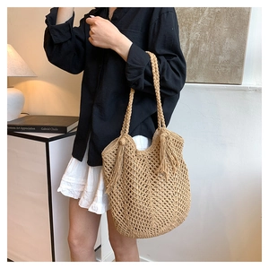Detail of woven straw tote bag featuring decorative tassels and textured knit pattern