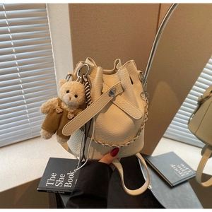 Chic cream white bucket bag with pebble leather texture, plush bear charm, and silver chain