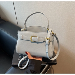 Détail du sac à main gris clair texture litchi avec boucles dorées et poignée haute