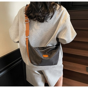 Detail of black nylon crescent bag with caramel strap and silver buckle on model