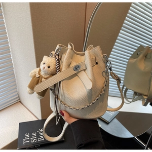 Detail of off-white bucket bag featuring lychee texture, bear charm and silver chain strap