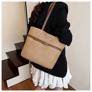 Detail of woven straw tote bag with brown leather strap worn by a model on stairs