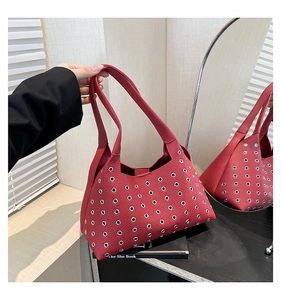 Detail of red leather shoulder bag with decorative silver grommets and long handle