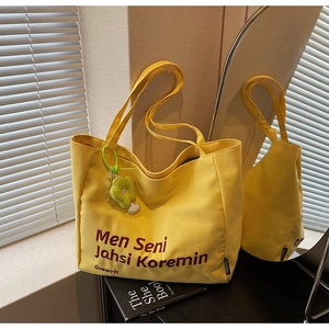 Close-up of yellow canvas tote bag with lettering and a floral charm accessory