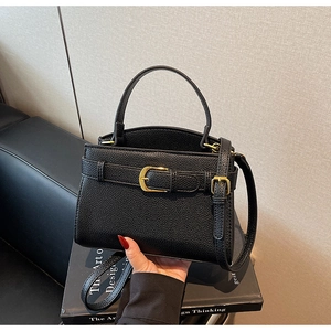 Détail d'un sac à main noir en cuir litchi avec boucle dorée et poignée élégante