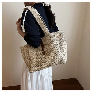 Détail d'un sac cabas en paille tissé avec sangle en cuir marron et anneaux dorés