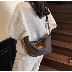 Detail of dark brown nylon crossbody bag with vibrant orange leather trim and wide shoulder strap