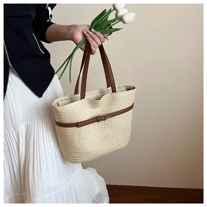 Detail of hand-woven straw tote bag with brown leather straps and metallic buckle accents