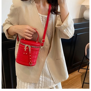 Detail of red quilted bucket bag with gold zippers and studs worn by a model in beige suit
