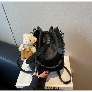 Close-up of black pebble leather bucket bag with cute plush bear charm and chain strap