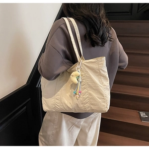 Detail of beige pleated fabric tote bag with a cute yellow moon plush pendant accessory