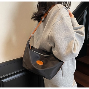Detailed side view of black Oxford fabric dumpling bag with orange leather logo and brown strap