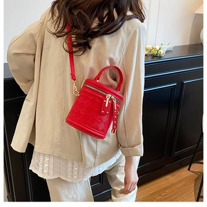 Close-up of red mini bucket bag with quilted texture and golden zippers worn over beige blazer