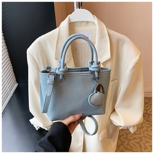 Detail of light blue bucket bag with leather texture and heart-shaped charm accessory